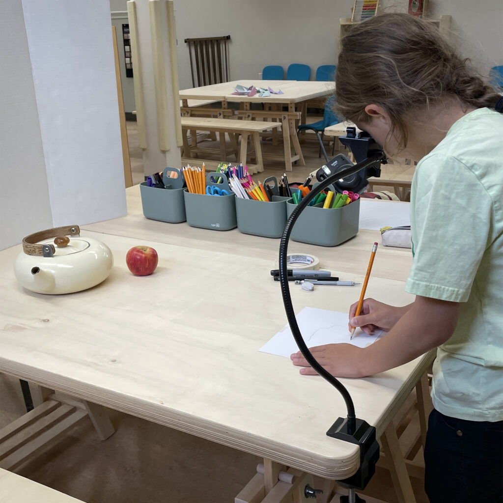 A 9-year-old child draws while using a camera lucida during a free community workshop. Preschool and After school Care in Cochrane AB