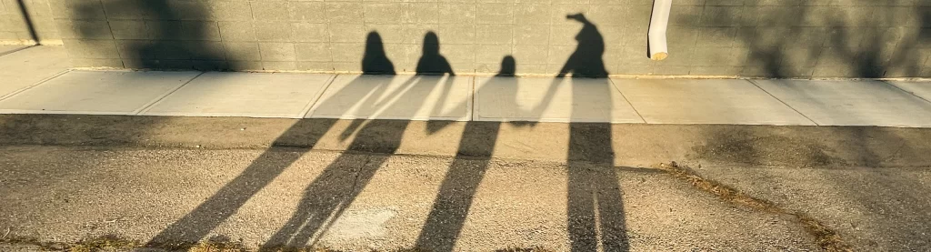 Children holding hands as sunlight casts their shadows on the ground and wall